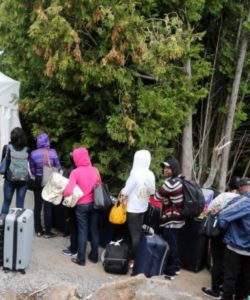 A line of asylum-seekers who said they were from Haiti wait to enter into Canada from Roxham Road in Champlain, New York, Aug. 7, 2017.