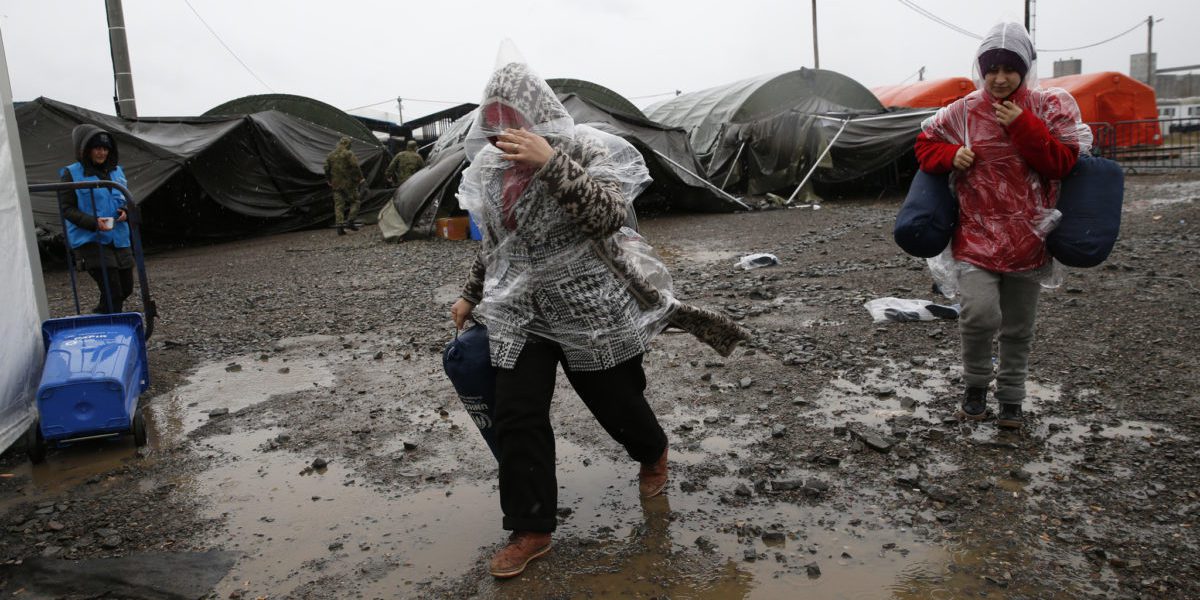 Unos migrantes corren bajo la lluvia hacia la tienda de campaña en la que se distribuye la ayuda mientras migrantes y refugiados esperan para continuar su viaje en tren a Europa occidental en un campamento de tránsito de refugiados en Slavonski Brod, Croacia.