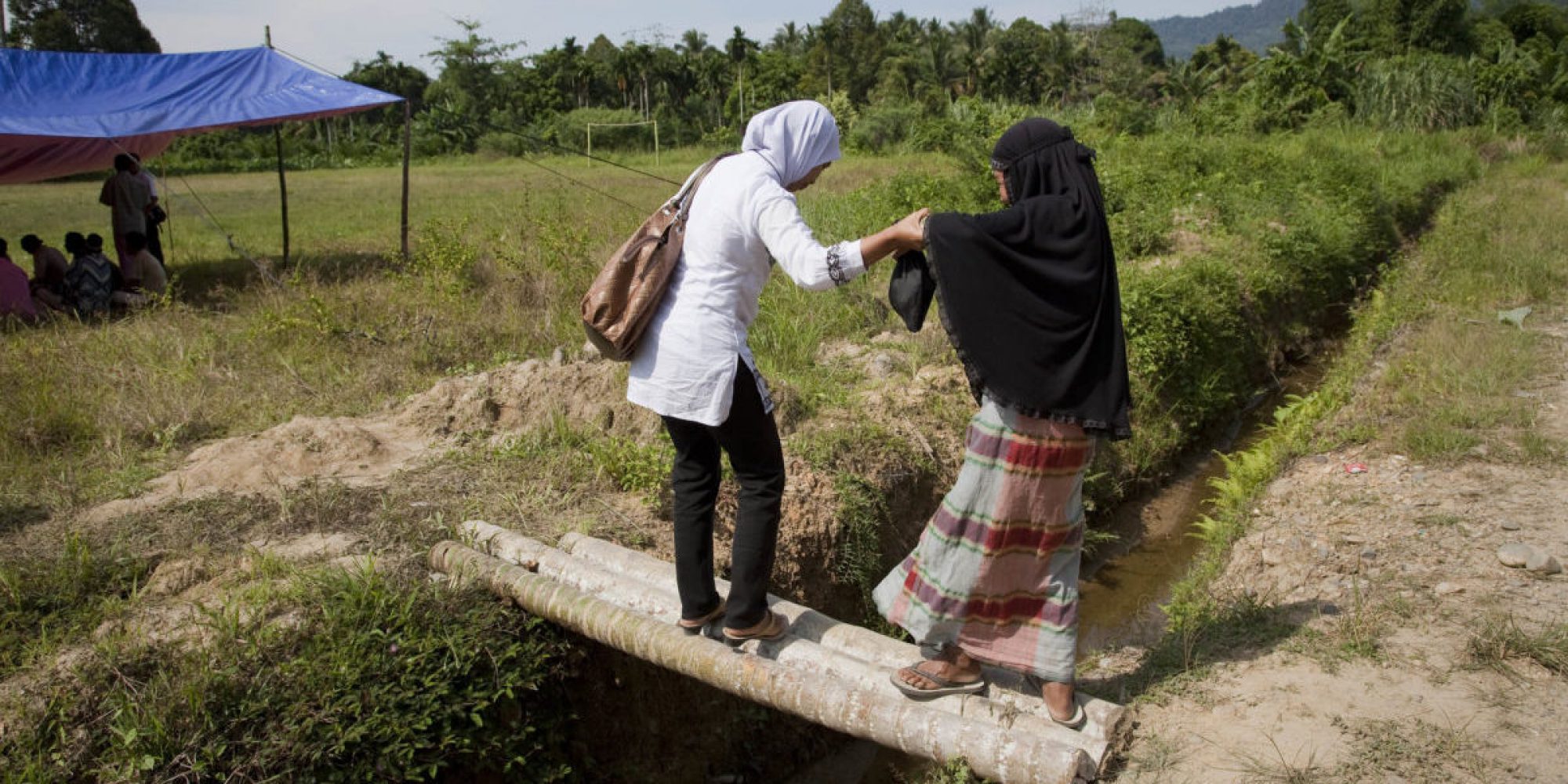 El miembro del equipo de JRS Indonesia asiste a una mujer que cruza el puente de bambú.