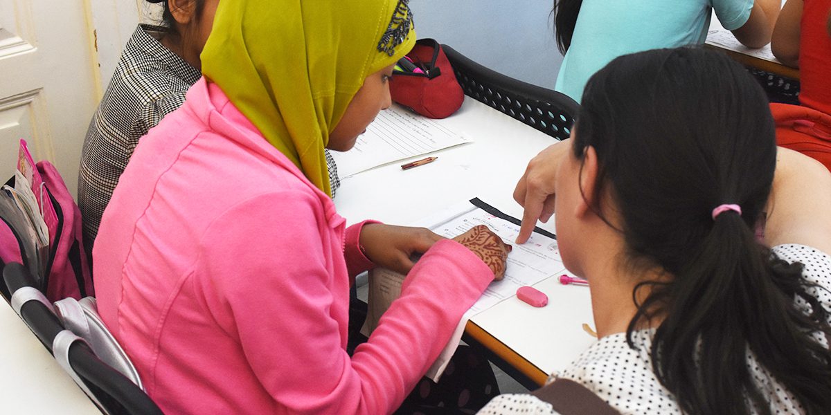 Une jeune femme reçoit de l’aide d’un enseignant dans sa classe au Centre Arrupe à Athènes (JRS)