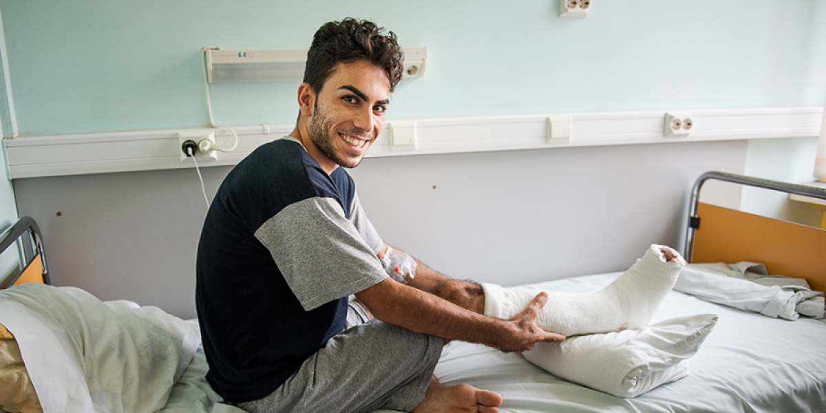 Mohamad sourit dans son lit d’hôpital après la deuxième opération pour guérir sa jambe blessée, à Bucarest, Roumanie (JRS)