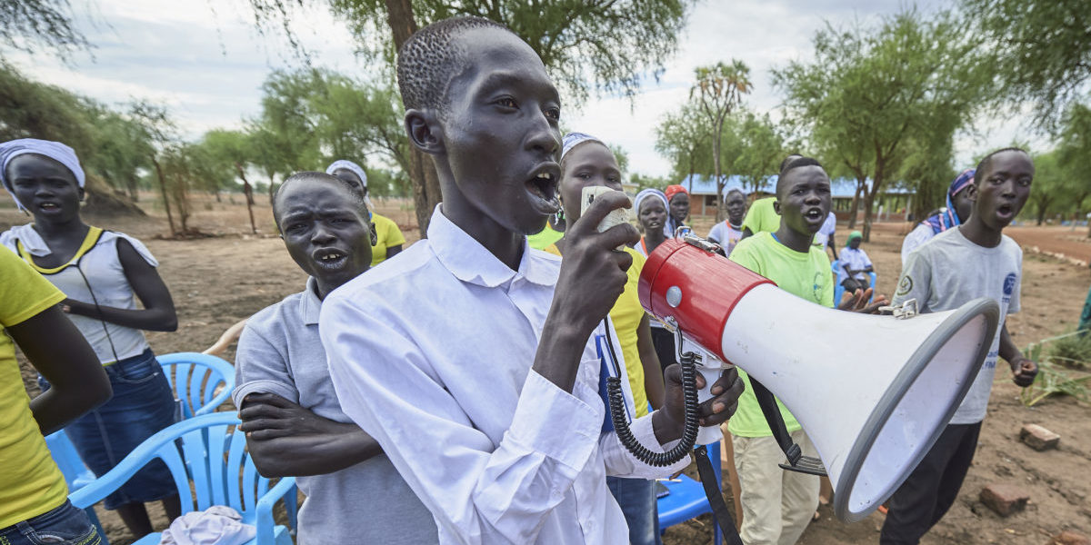 Avec un mégaphone, un homme conduit un groupe de réfugiés chantant pendant une activité sponsorisée par JRS dans le camp de réfugiés de Doro à Maban, Soudan du Sud.