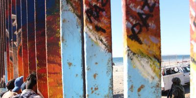 Migrants at the border between Tijuana and San Diego. The border fence is painted with the word