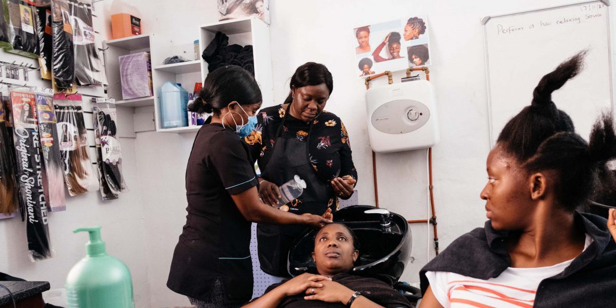 Beauty course instructor Abimbola Adeola demonstrates how to perform a hair-relaxing procedure to, from left, Mira Okito, Myriam Nkulu and Jean Dalc at the Jesuit Refugee Service's skills development centre in Pretoria. (James Puttick / New Frame)