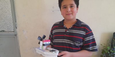 Amro, un réfugié syrien et étudiant du JRS Baalbek, pose fièrement avec l'une de ses inventions : un bateau alimenté par des piles.