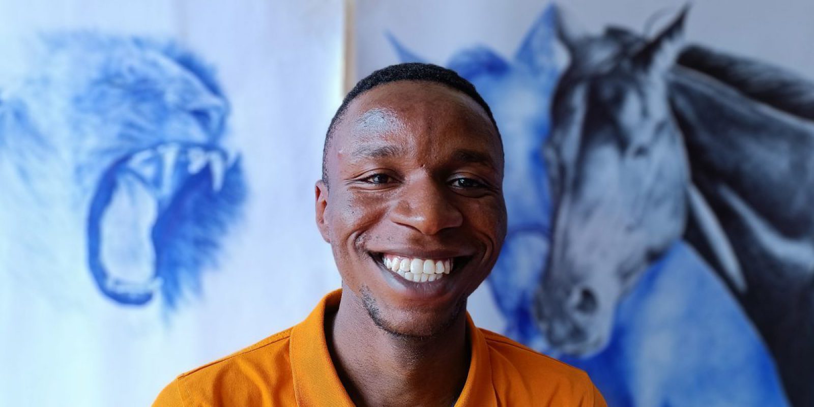 Serge, refugee and pen artist poses with his drawings in the background. Serge is a Congolese refugee and pen artist living in Uganda, where he was sponsored by JRS to pursue his studies and become an engineer.